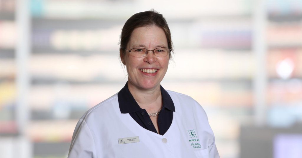 Barbara Göring, eine lächelnde Frau mit Brille und weißem Laborkittel, steht vor einem unscharfen Hintergrund. Sie hat ihr braunes Haar zurückgebunden und trägt unter dem Laborkittel ein dunkles Hemd mit Kragen.