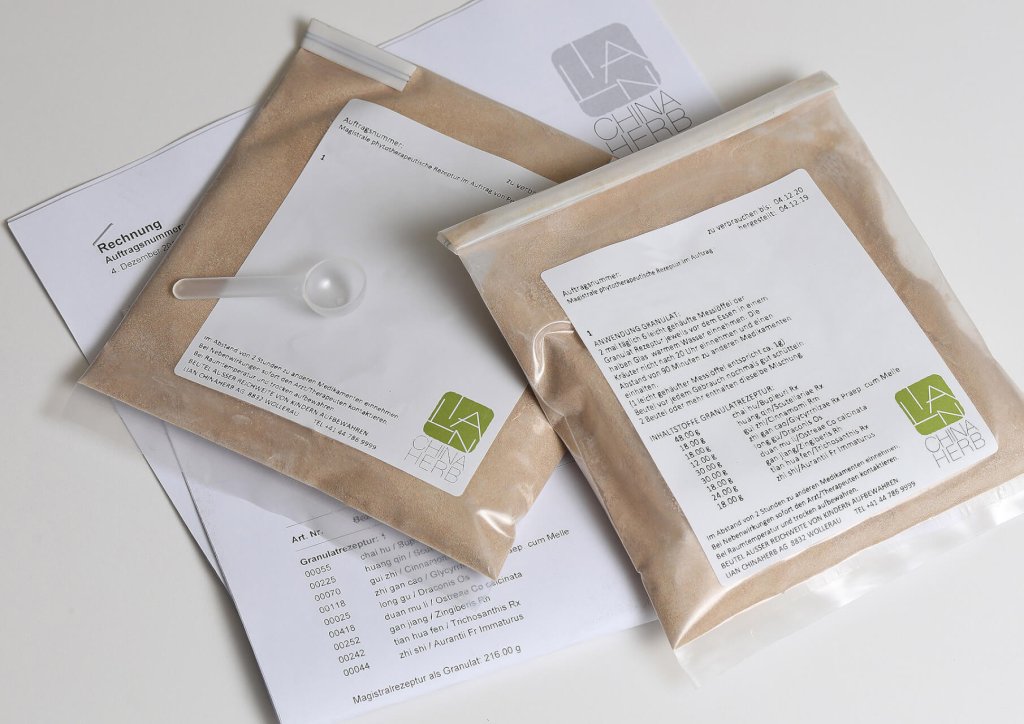 Zwei durchsichtige, mit hellbraunem Pulver gef&uuml;llte Plastikbeutel, die jeweils mit Text und dem gr&uuml;nen LA China Herbs-Logo beschriftet sind, liegen auf Papieren. Auf einem Beutel ruht eine kleine Schaufel - perfekt f&uuml;r Ihren TCM Abholservice in der Traditionellen Chinesischen Medizin.