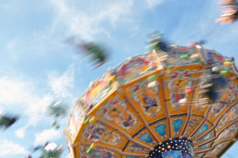 Eine farbenfrohe, sich drehende Karussellfahrt in einem Vergn&uuml;gungspark, aufgenommen mit Bewegungsunsch&auml;rfe vor einem blauen Himmel mit leichten Wolken, ruft Aufregung und den schwindelerregenden Rausch des Schwindels hervor.