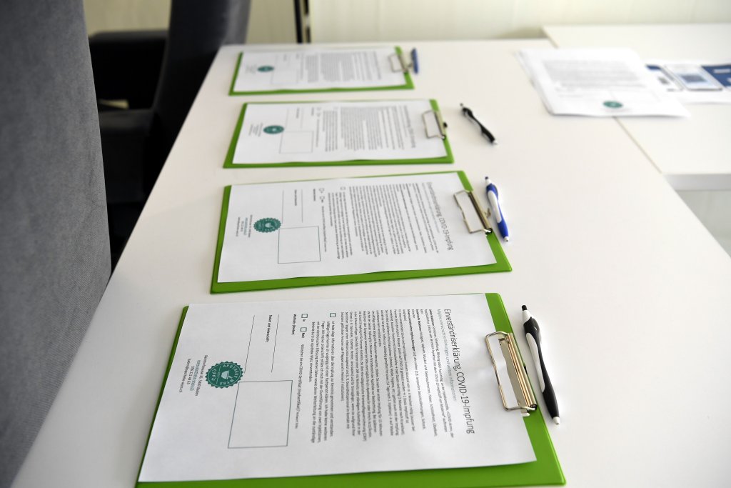 Vier gr&uuml;ne Klemmbretter mit bedruckten Formularen und Stiften sind ordentlich auf einem wei&szlig;en Tisch angeordnet, was auf eine Registrierung oder Anmeldung bei DGS-Besuch hindeutet, m&ouml;glicherweise f&uuml;r die COVID-19-Impfung oder eine offizielle Zustimmung.