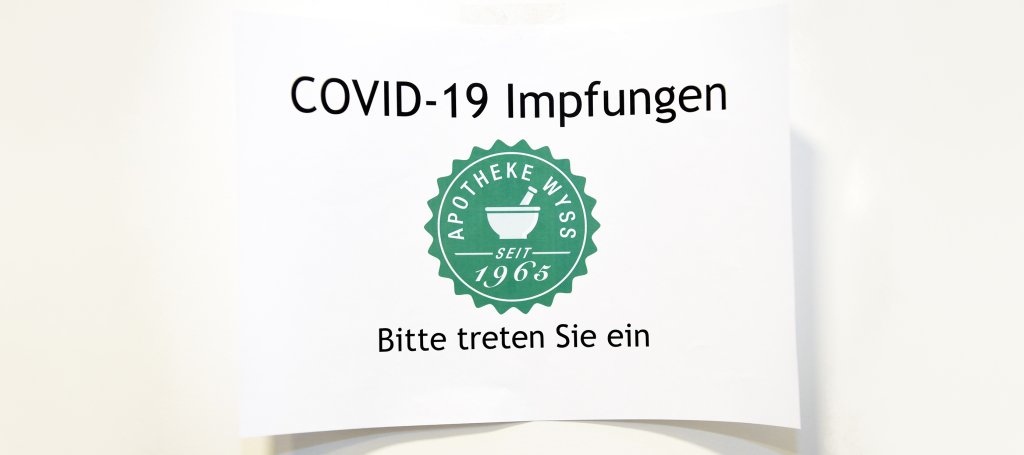 Ein Schild mit der Aufschrift COVID-19 Impfungen, darunter das Logo der Apotheke Wyss und der Text Bitte treten Sie ein und laden Ihren Besuch ein. DGS-Informationen können auch für die Zugänglichkeit verfügbar sein.