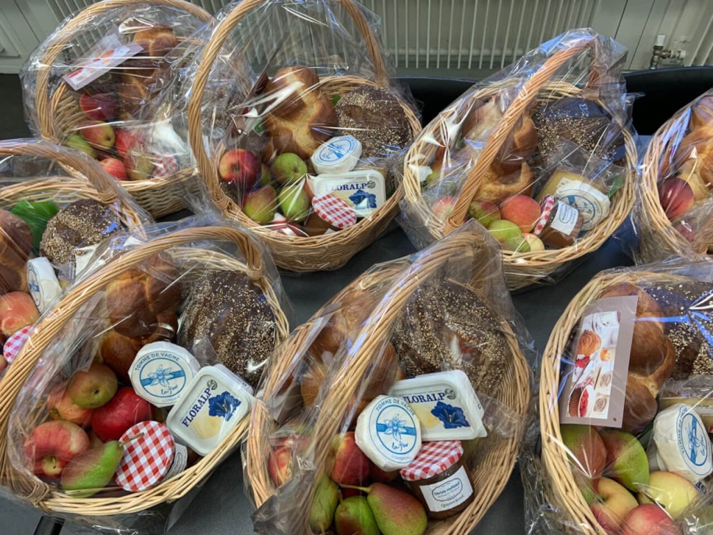Mehrere in Plastik eingewickelte Weidenk&ouml;rbe mit &Auml;pfeln, Birnen, Br&ouml;tchen, einem Glas Konfit&uuml;re und K&auml;se stehen auf einem Tisch zum 15-j&auml;hrigen Jubil&auml;um im T&auml;fernhof D&auml;ttwil.