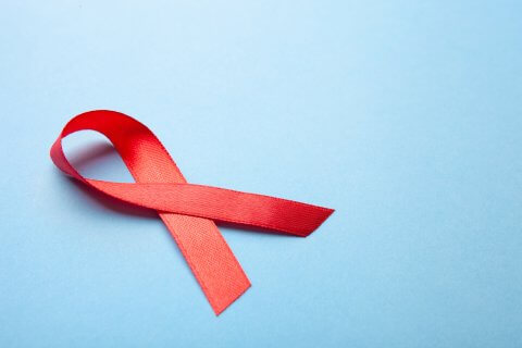 Ein rotes Band, das gemeinhin mit HIV/AIDS assoziiert wird, liegt auf einem hellblauen Hintergrund.