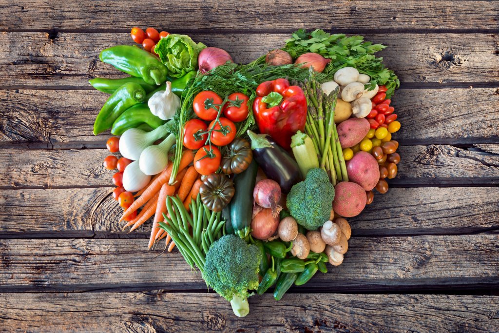 Eine Vielzahl von frischem Gem&uuml;se, darunter Tomaten, Brokkoli, Karotten, Paprika, Pilze und mehr - perfekt f&uuml;r ein von Sch&uuml;ssler Salz inspiriertes Gericht - sind in Form eines Herzens auf einer rustikalen Holzfl&auml;che angeordnet.