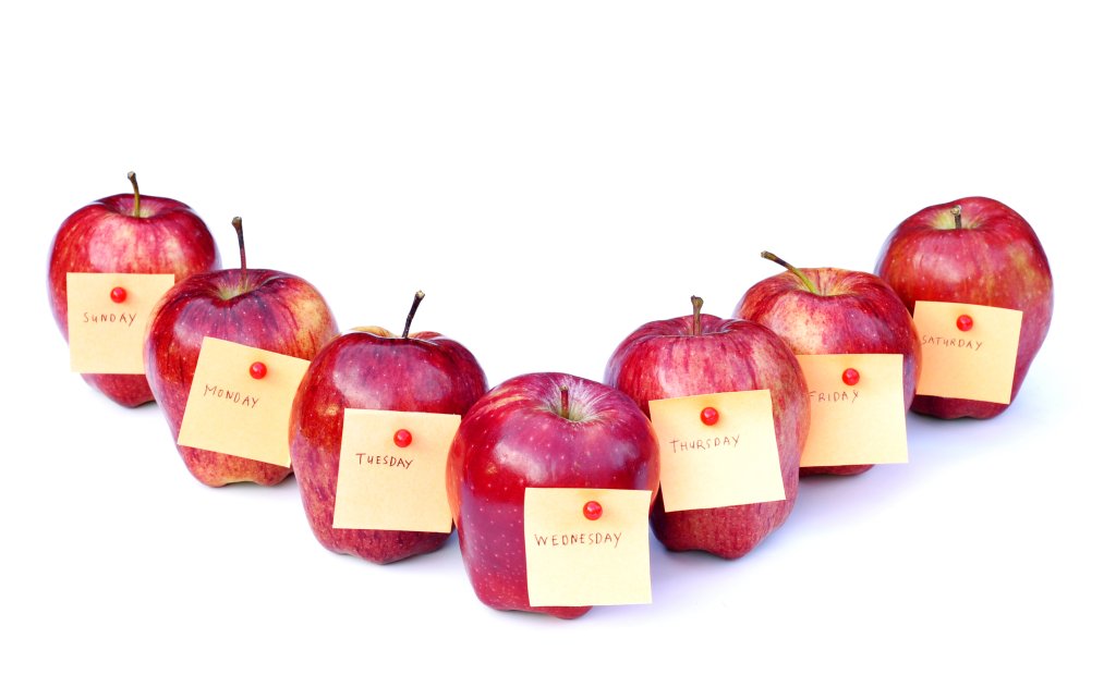 Sechs rote &Auml;pfel, die jeweils mit einem Wochentag beschriftet sind, reihen sich auf wei&szlig;em Hintergrund aneinander und erinnern daran, sich auf die Gesundheit zu konzentrieren und intelligente Wege zu finden, um Pr&auml;mien bei den Krankenkassen-Pr&auml;mien 2024 zu sparen.