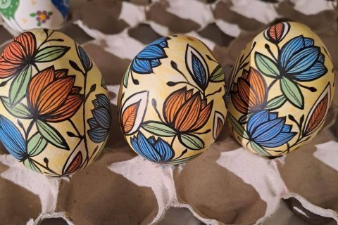 Drei Ostereier, verziert mit nat&uuml;rlicher Farbenpracht in roten, blauen, gr&uuml;nen und schwarzen Blumenmustern, stehen auf einem Papptablett. Die kr&auml;ftigen Bl&uuml;ten und Bl&auml;tter fangen den Geist des gesunden Ostern ein.