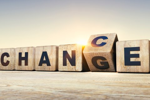 Holzkl&ouml;tze buchstabieren CHANGE, wobei der Buchstabe G umgedreht wird, um CHANCE zu bilden, was einen Perspektivenwechsel vor dem Hintergrund eines Sonnenaufgangs oder Sonnenuntergangs symbolisiert.