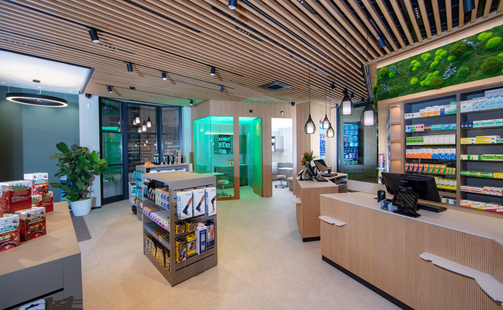 Das moderne Interieur der Apotheke Wyss in der N&auml;he des Bahnhofs Baden zeichnet sich durch helle Holzeinbauten, Regale mit Gesundheitsprodukten, zwei Kassen, einen beleuchteten Beratungsraum und Pflanzen aus, die dem hellen Raum eine nat&uuml;rliche Note verleihen.