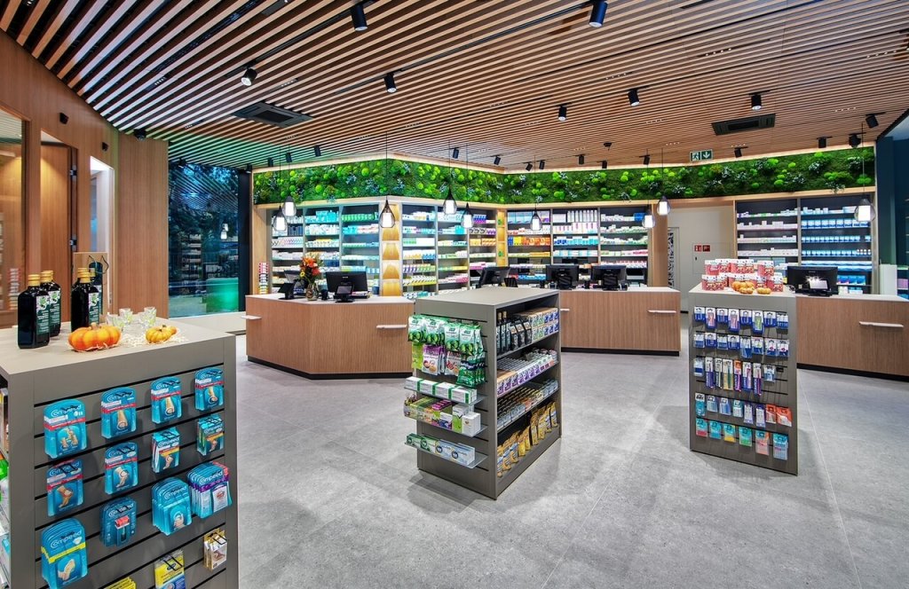 Modernes Apothekeninterieur in der Apotheke Wyss beim Bahnhof Baden mit Holzdecken, hellen Regalen mit Medikamenten und Gesundheitsprodukten, Grünpflanzen an der Rückwand und grosszügigen Auslagen für rezeptfreie Artikel.