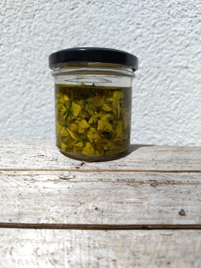 Ein Glasgef&auml;&szlig; mit schwarzem Deckel und der Aufschrift "Automatisch gespeicherter Entwurf" ist mit gelben Blumen und &Ouml;l gef&uuml;llt und steht auf einer rustikalen Holzfl&auml;che vor einem wei&szlig; strukturierten Hintergrund.