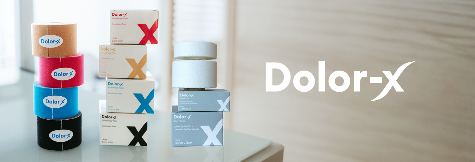 Auf einer wei&szlig;en Fl&auml;che stapeln sich Schachteln und Rollen von Dolor-X-Sportband in verschiedenen Farben und Gr&ouml;&szlig;en. Das Dolor-X-Logo erscheint gut sichtbar auf der rechten Seite des Bildes.