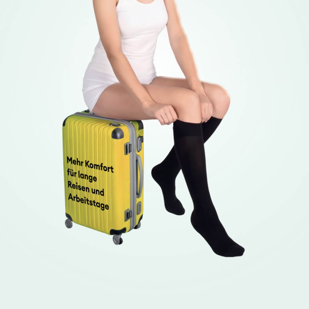 Eine Frau in wei&szlig;er Kleidung sitzt auf einem gelben Koffer mit der Aufschrift &bdquo;Mehr Komfort f&uuml;r lange Reisen und Arbeitstage&ldquo; und tr&auml;gt schwarze Kompressionsstr&uuml;mpfe f&uuml;r &bdquo;leichte Beine beim Reisen&ldquo;.